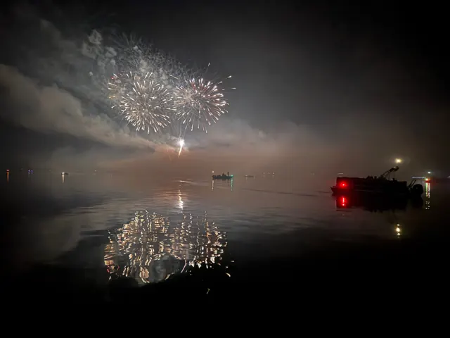 Fireworks reflected on Lake Arbutus beside pontoons and boats.