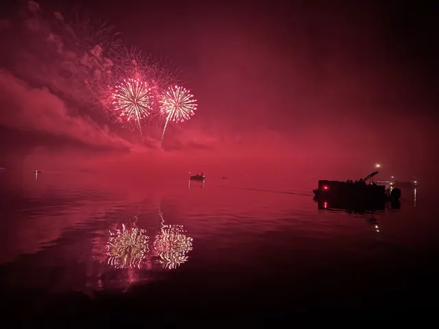 Red fireworks lighting up Lake Arbutus with bright reflections on the water.
